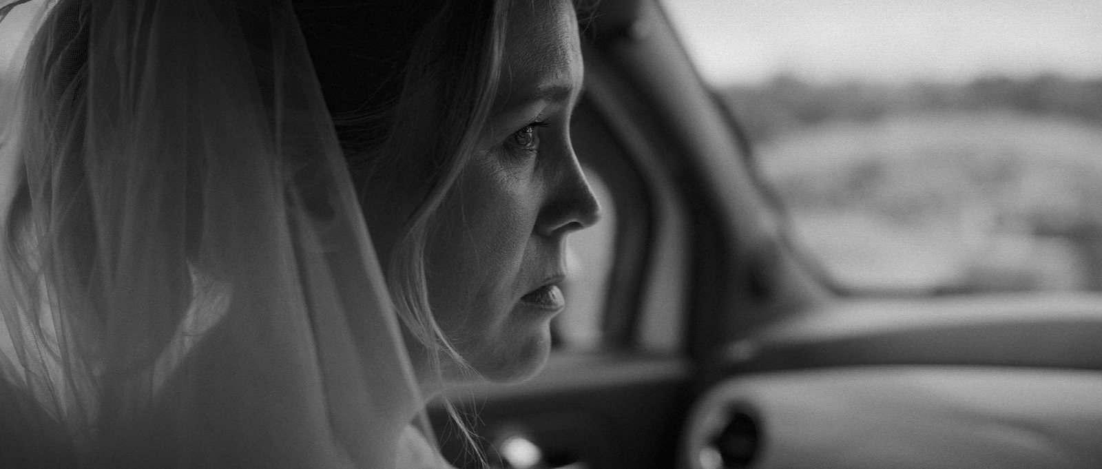 Woman in a wedding dress holding a MARRY ME sign at the roadside, black-and-white frame